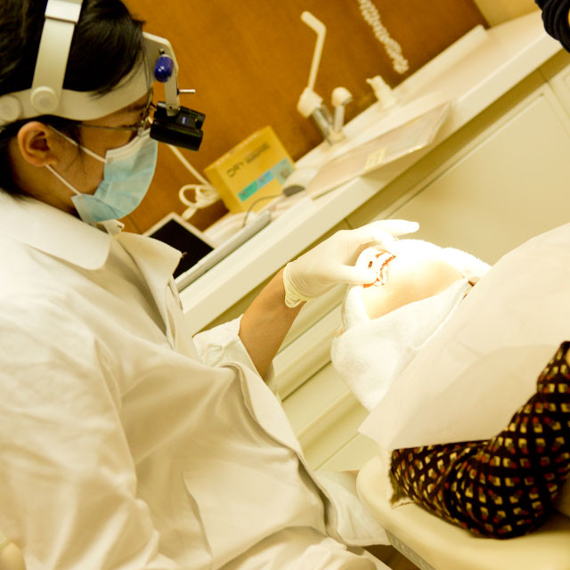 歯科診察台に横になっている高齢者の口を開けて歯の状態を確認する歯科医師